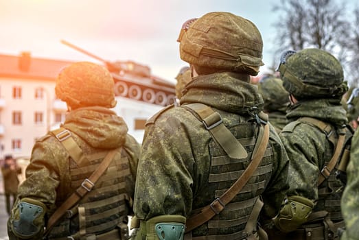 Several soldiers wearing camouflage uniforms stand in a row, holding guns and looking prepared for a mission. The background is blurred, highlighting their readiness and determination.