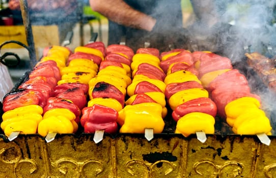 Colorful bell peppers on skewers grilling outdoors, sizzling and charred. A delicious smoky aroma fills the air, creating a vibrant and appetizing scene for a summer barbecue gathering.