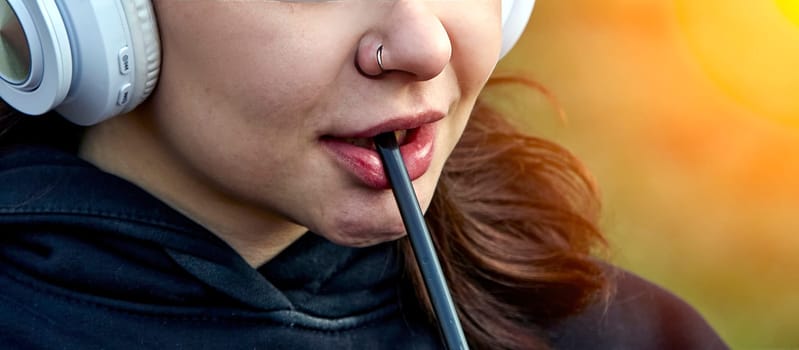 A close-up shot of a young woman wearing headphones, biting on a straw. Her face is relaxed, suggesting a moment of peace and quiet.