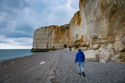 etretat,france,23-04-2024, woman walking on the beach at the famous calck cliffs in normandy france near etretat, view from the beach