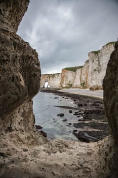 Landscape photo of tall, steep limestone cliffs by the ocean with one with a hole in it creating an arch view from the beach