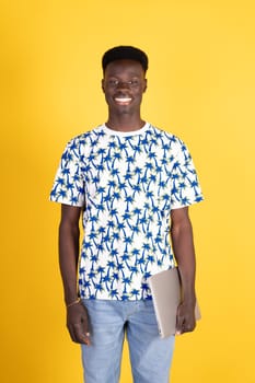 A young man wearing a shirt with palm trees on it is holding a laptop. He is smiling and he is happy