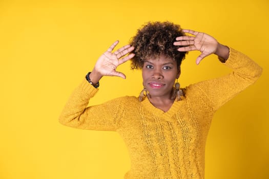 Young pretty smiling black woman showing palms with curly afro hair, wearing yellow sweater on yellow background, with copy space. Happiness concept.