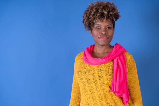 A woman dressed in a yellow sweater and a pink scarf, standing with a neutral expression.