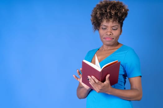 Young black woman reading a book wearing a blue dress on a blue background with copy space. Concept studying.