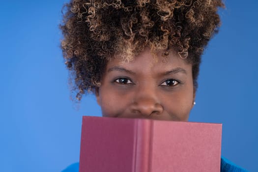 A woman holds a pink book over her face, partially covering her features.