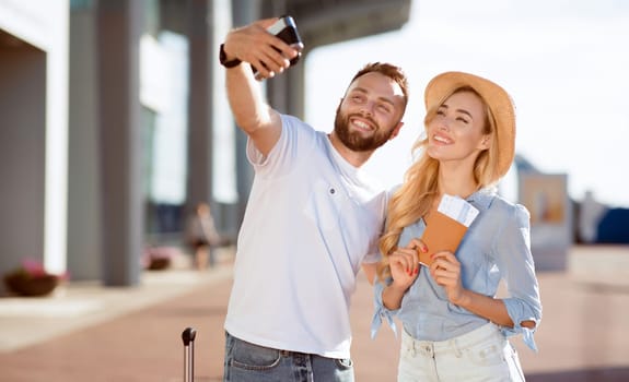 Vacation Begins. Happy couple taking selfie with tickets using camera, waiting for a flight near the airport building