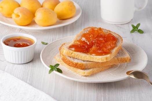 Apricot jam on bread in a white plate and a jar of apricot jam.