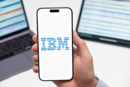 PRAGUE, CZECH REPUBLIC - JANUARY 21 2024: IBM logo on the screen of smartphone in mans hand on the workplace background.