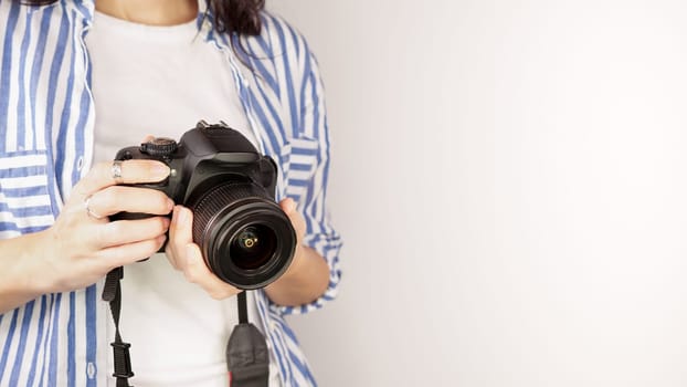 Photographer holding dslr camera. Self portrait, front view. Faceless nice woman with brown red hair in a tshirt with hands holding photo camera white background