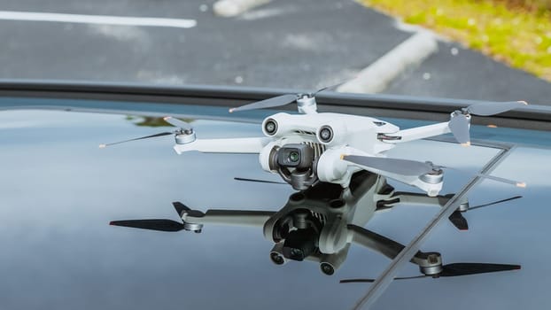 A sleek white quadcopter drone with four propellers is perched on the roof of a shiny black car against a blurred urban background, showcasing technology and innovation.