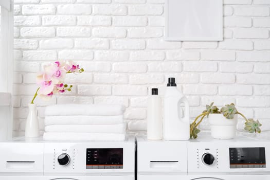 Two white front loading washing machines sit side by side in a laundry room with a white brick wall background.