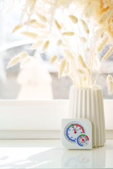 A white windowsill with dried flowers in a white vase and a glass vase.