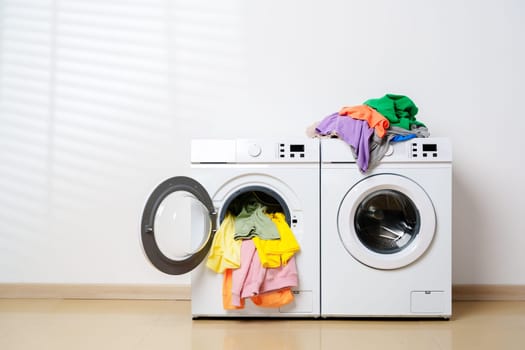 A white washing machine with a glass door open, revealing colorful clothes spilling out of the machine.