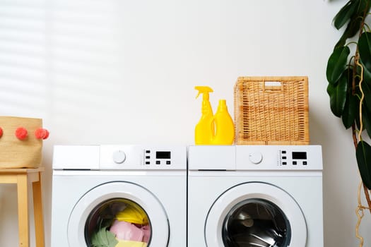 A white washing machine sits in a laundry room with yellow cleaning supplies on top.