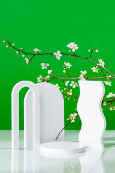 Decorative podiums and blooming branches on green background with shadows copy space