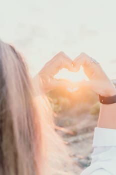 A woman's hand is holding a heart shape, with the sun shining on it. Concept of love and warmth, as the sun symbolizes happiness and positivity. The heart shape represents the bond between two people