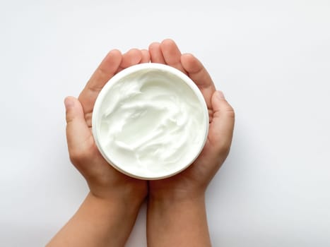 Close up of childs hands holding container of hand cream on white background. Skincare and moisturizing concept. Design for healthcare, beauty, wellness, and child care poster. High quality photo