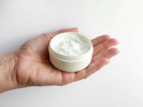 Close up of middle age woman hand holding container of hand cream on white background. Skincare and moisturizing concept. Design for healthcare, beauty, wellness, and self care poster. High quality