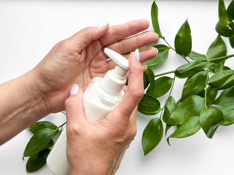 Close up of middle age woman hands dispensing lotion from bottle with green leaves on white background. Skincare and natural beauty concept. For healthcare, wellness, and organic product poster.