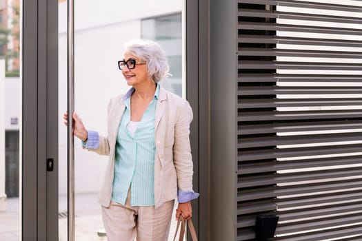 smiling mature woman coming out of the home portal, concept of happiness and active lifestyle in adulthood, copyspace for text