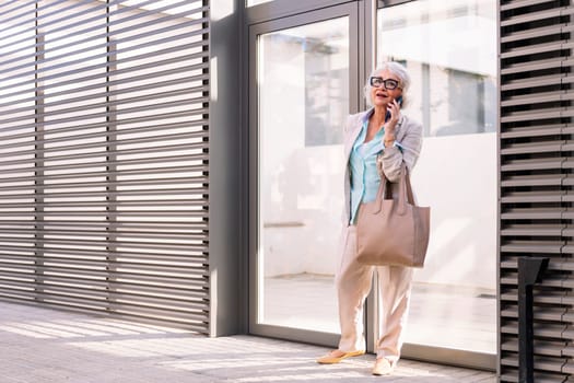 smiling mature woman coming out of the home portal while talking on mobile phone, concept of happiness and technology of communication, copyspace for text
