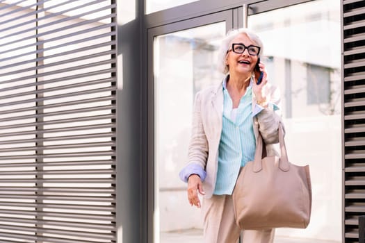 smiling mature woman coming out of the home portal while talking on mobile phone, concept of happiness and technology of communication, copyspace for text