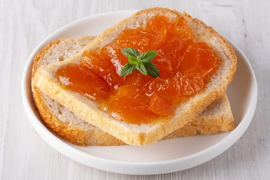 Toasted bread with apricot jam and mint on a white wooden table. Tasty breakfast.