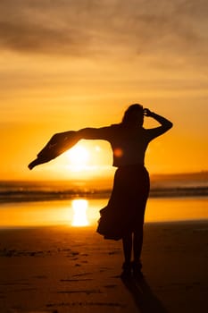 A woman stands on a beach with her arms outstretched, looking up at the sun. Concept of freedom and joy, as the woman is enjoying the moment and embracing the beauty of the sunset