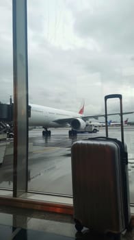 Inside the airport, a suitcase stands before a window, framing a departing airplane against a cloudy sky. The scene encapsulates the essence of travel and the lure of the unknown
