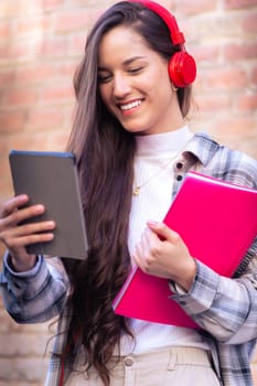 Young smiling student with notebook in hand uses social networks with tablet applications and wireless technology outdoors.