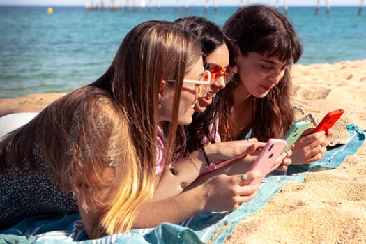 Three young women using apps on their cell phones on the beach