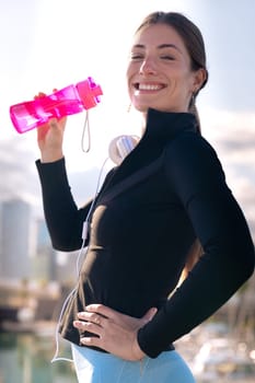 athletic woman smiling drinking water while exercising looking at camera