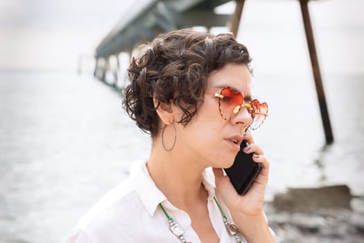 woman with sunglasses on vacation on the beach, talking on mobile phone.
