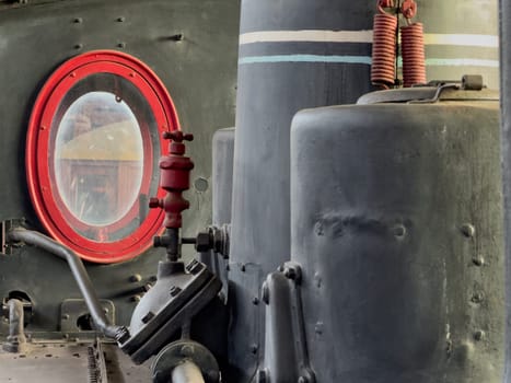 Interior of an old locomotive's cab showing industrial details and a red window frame.