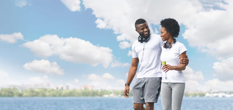 Joyful Black Couple Hugging And Walking Along River Bank After Morning Run. Panorama, Empty Space