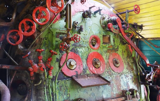 An old steam boiler with controls in the cabin of an abandoned, non-working retro locomotive. Equipment from taps, valves, levers.