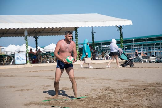 young guy in black shorts serves the ball while playing beach volleyball on the sea during vacation, ball matches and active activities, Green Max Hotel,Belek, Turkey, May 31, 2024