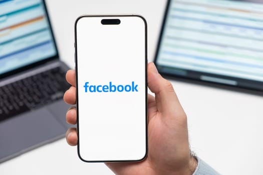 PRAGUE, CZECH REPUBLIC - JANUARY 21 2024: Facebook logo on the screen of smartphone in mans hand on the workplace background.