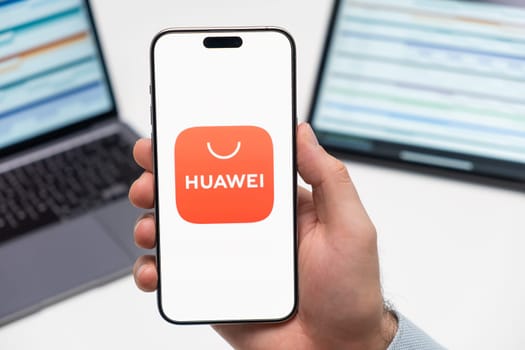 PRAGUE, CZECH REPUBLIC - JANUARY 21 2024: Huawej logo on the screen of smartphone in mans hand on the workplace background.