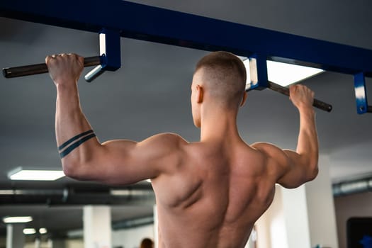 Bodybuilder performs a pull-up exercise at a gym, showcasing his muscular back