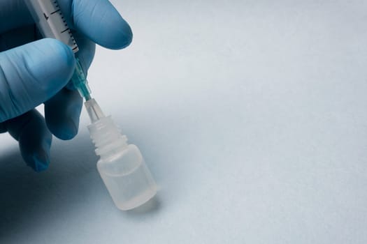 Taking medication with a syringe. A man's hand in a blue glove close-up holds a syringe inserted with a needle into a plastic bottle.