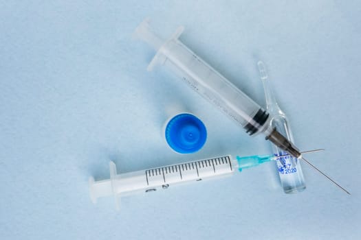 Two syringes and two vials of medicine on a blue background, top view.