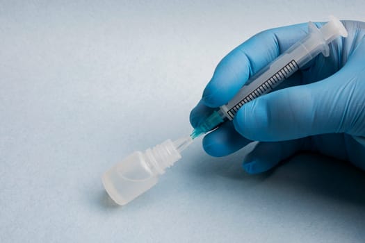Close-up of a doctor's hand in a blue glove inserting a syringe into a bottle of medicine on a blue background.