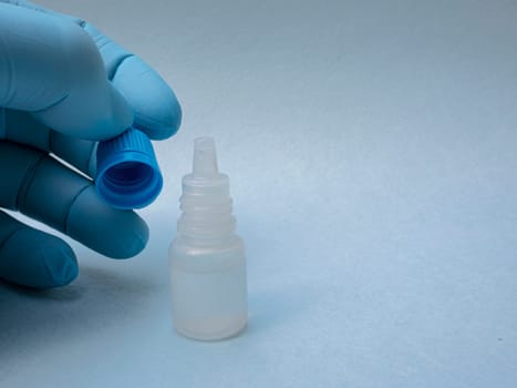 A man's hand in a blue glove close-up holds the cap of a plastic bottle with medicine close-up.