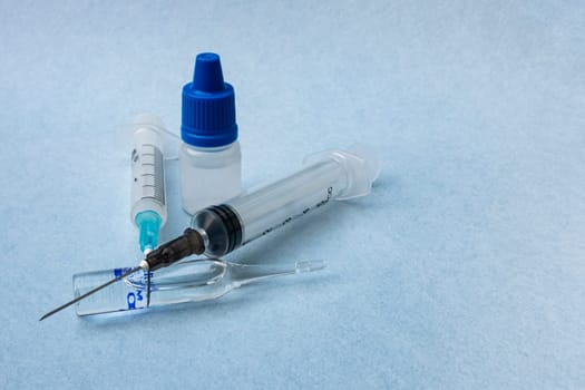 Two syringes, one glass ampoule with medicine, a plastic bottle with liquid close-up, on a blue background.