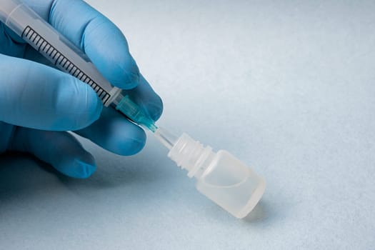 Close-up of a doctor's hand in a blue glove inserting a syringe into a bottle of medicine on a blue background.