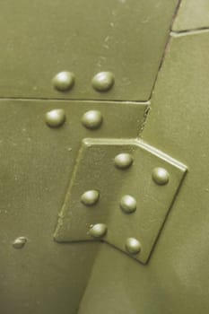 Close-up vertical photo of a fragment of armor with rivets of a protective shield from an artillery gun.
