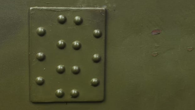 Photo of a fragment of armor with rivets of a protective shield of military equipment.