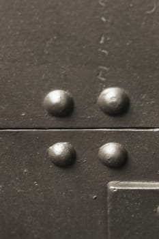 Close-up vertical photo of a fragment of armor with rivets of a protective shield from an artillery gun.